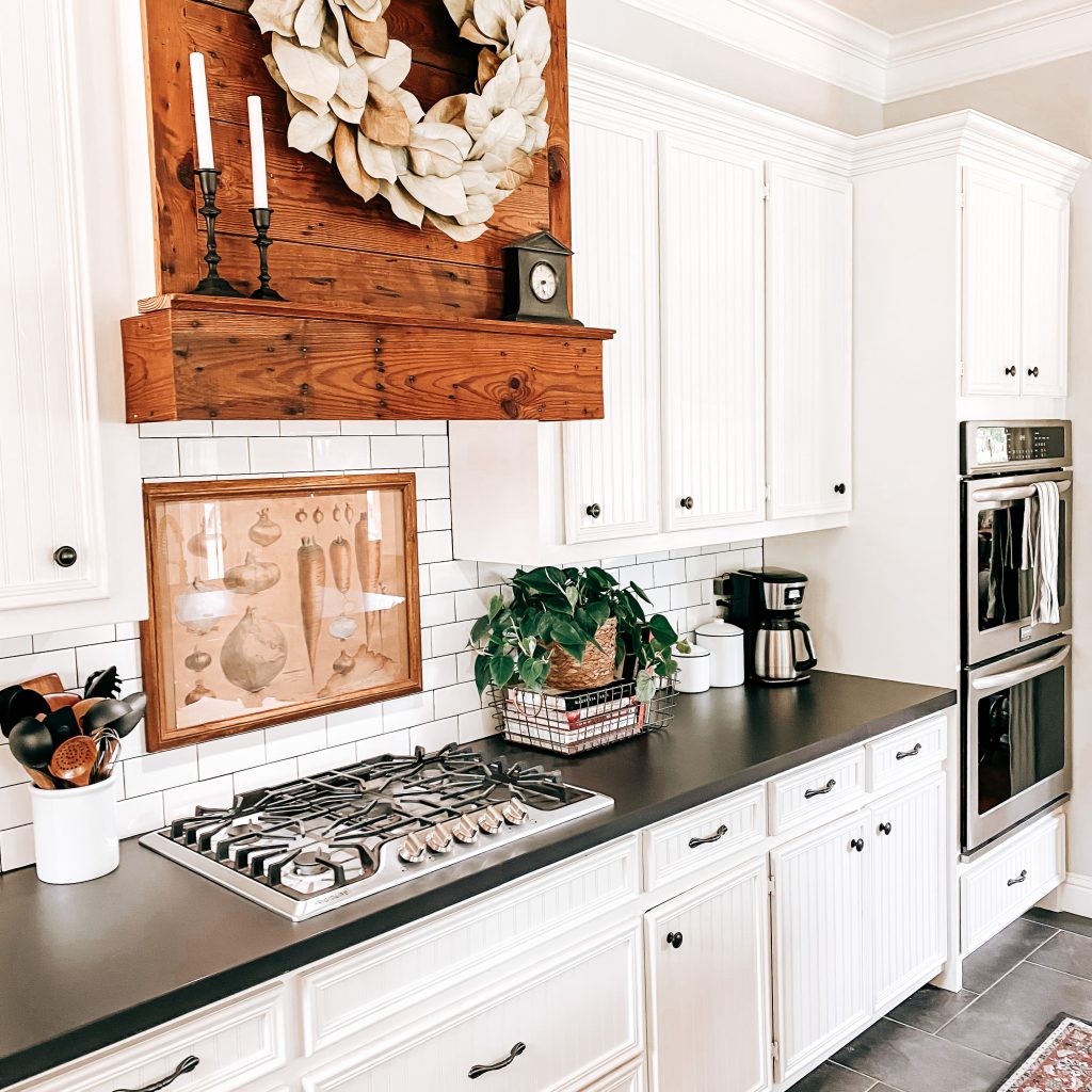 The Yellow Rose Farmhouse Kitchen with view of subway tile backsplash, barn wood range hood, pathos plant, vintage vegetable print, double oven and rustic farmhouse decor