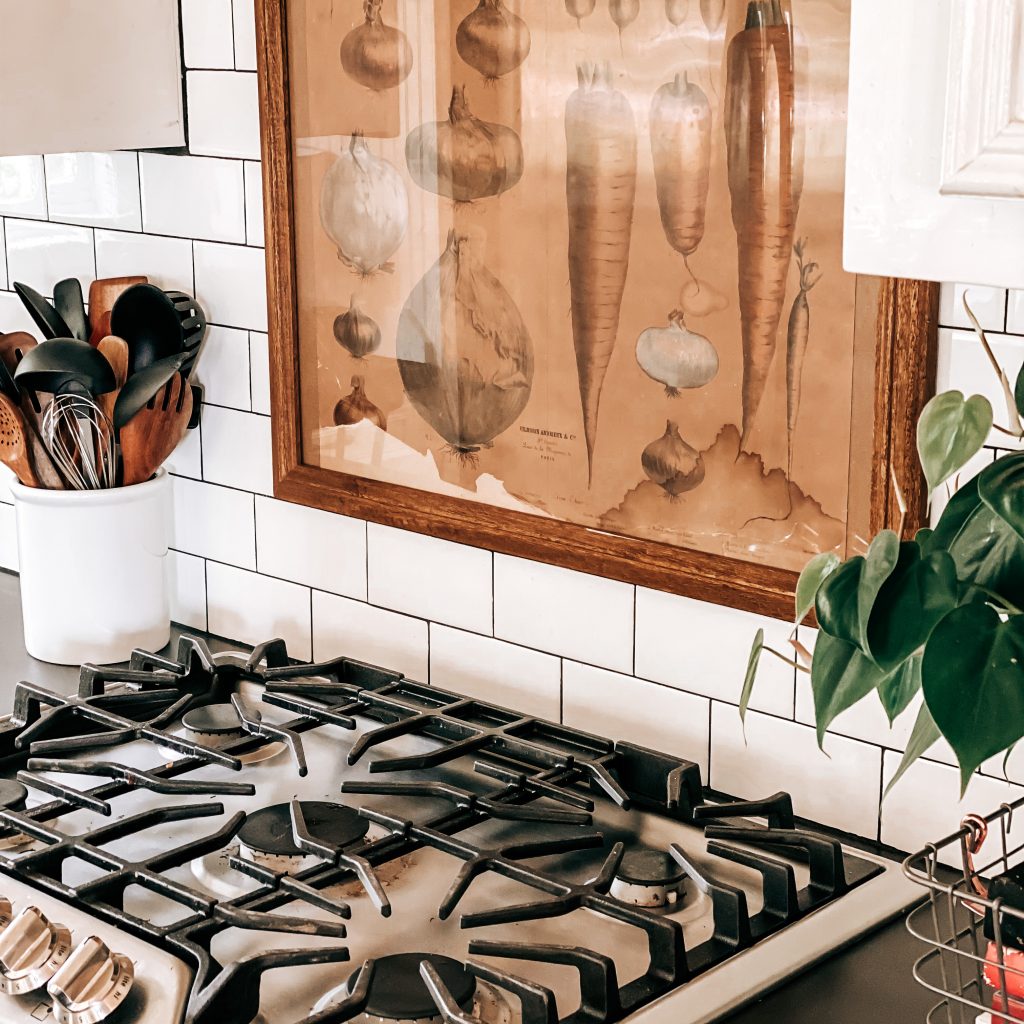 The Yellow Rose Farmhouse Kitchen Cooktop range with subway tile backsplash and vintage vegetable print in rustic wood frame