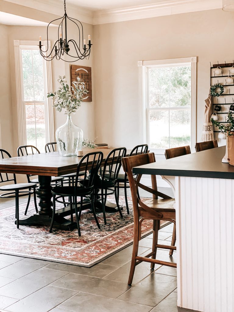 The Yellow Rose Farmhouse Kitchen and Dining Room with farmhouse table, bistro chairs, farmhouse counter stools, farmhouse washable rug, herringbone floor tile, mug rack, farmhouse wall decor and antique chandelier and other farmhouse accessories.