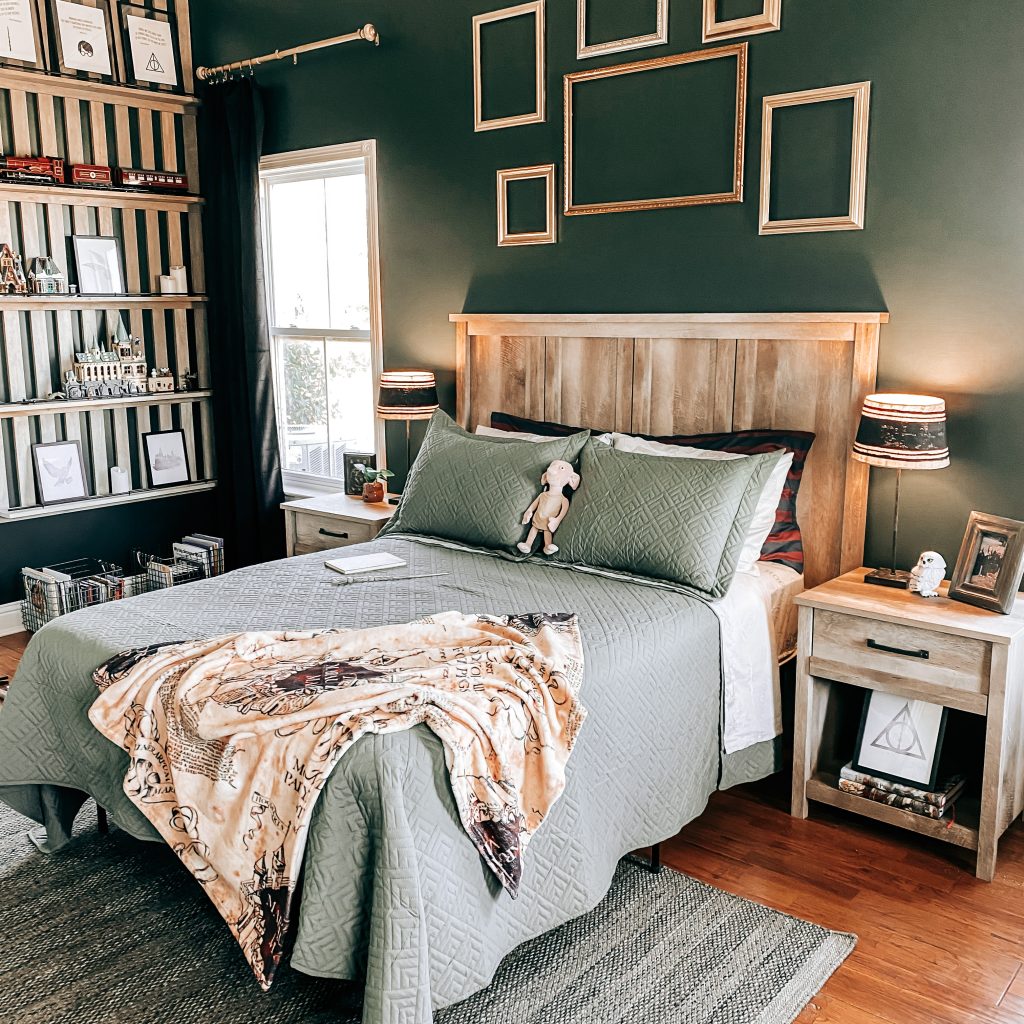 Side view of Harry Potter Themed bedroom and bed decorated with Slytherin bedding, marauder's map throw blanket and Dobby plush toy. There are gold frames staggered on the wall behind the bed that's painted with Behr paint in the color, Charcoal smoke. The nightstands have Harry Potter decor including Hedwig, a baby Mandrake, Tom Riddle's Diary and the Harry Potter books. The DIY Wood Slat Accent wall with shelves is to the side of the bed and it's decorated with more Harry Potter Decor and Legos | The Yellow Rose Farmhouse | www.theyellowrosefarmhouse.com