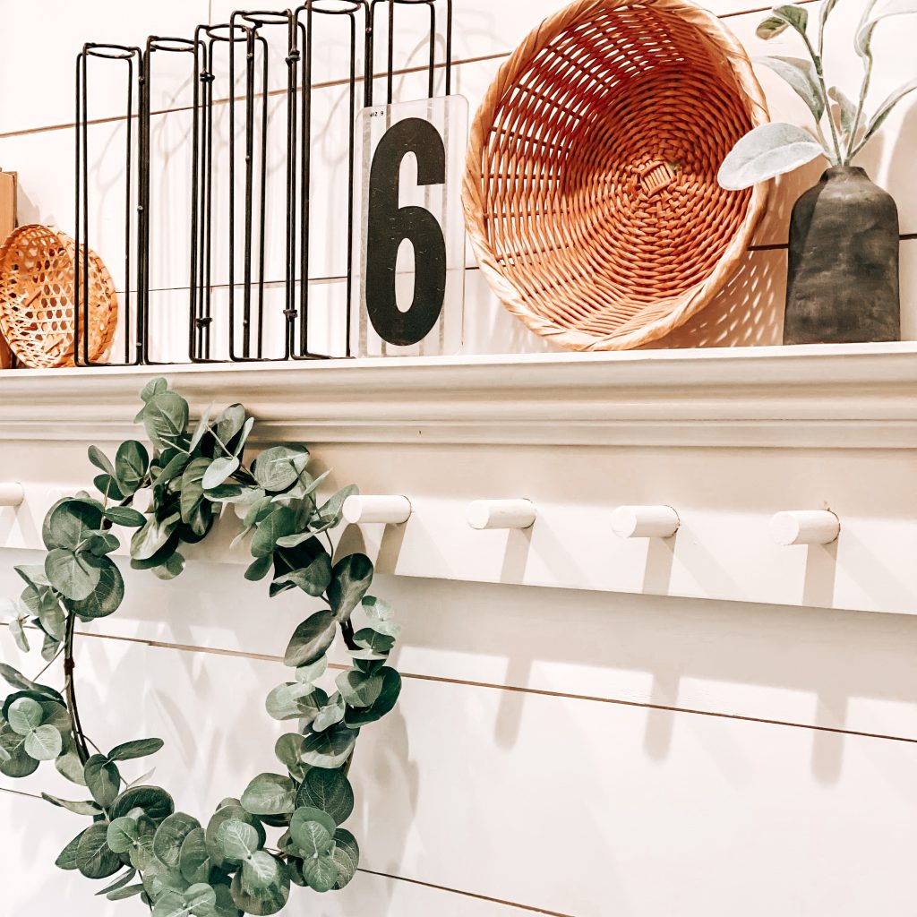 Close up of DIY Peg Shelf with farmhouse and antique decor like an antique frame, vintage books, boho wicker baskets, textured and distressed bud vase, wood bead garland and a eucalyptus wreath hanging from the peg | The Yellow Rose Farmhouse | www.theyellowrosefarmhouse.com