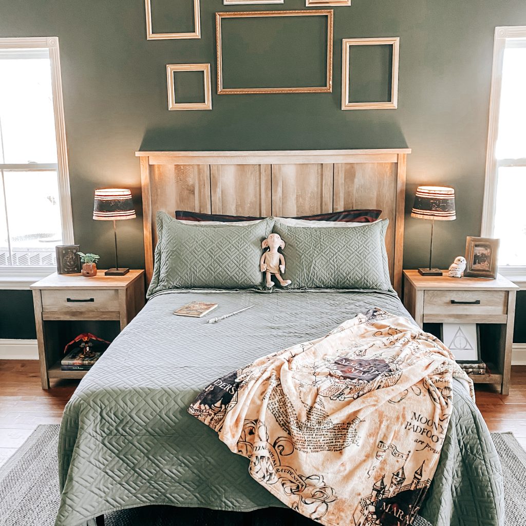 Front view of Harry Potter Themed bedroom and bed decorated with Slytherin bedding, marauder's map throw blanket and Dobby plush toy. There are gold frames staggered on the wall behind the bed that's painted with Behr paint in the color, Charcoal smoke. The nightstands have Harry Potter decor including Hedwig, a baby Mandrake, Tom Riddle's Diary and the Harry Potter books. | The Yellow Rose Farmhouse | www.theyellowrosefarmhouse.com