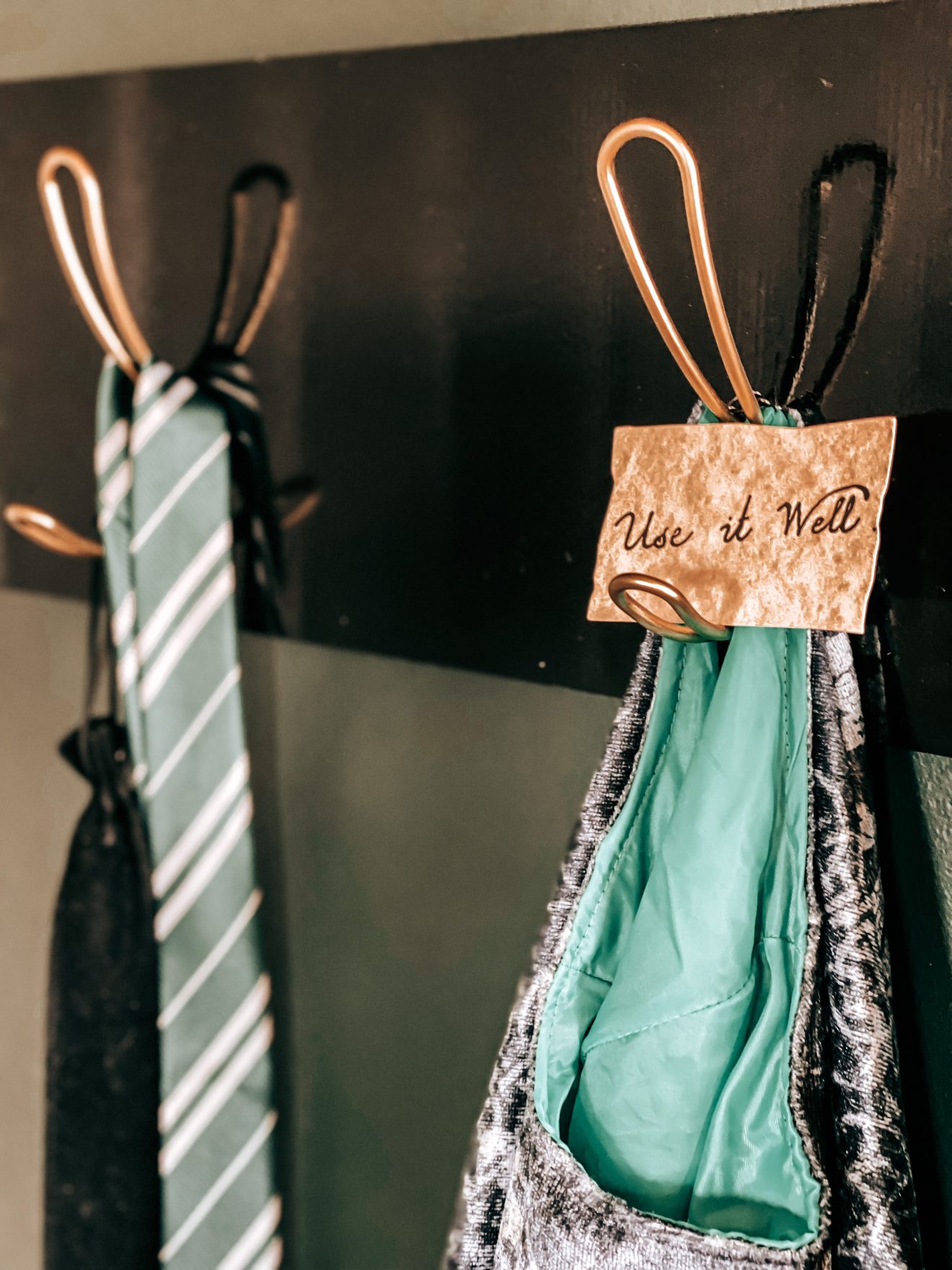 Close up of wall decorated with Harry Potter Glasses decal, Hogwarts crest banner flag and wall hooks that have a Slytherin tie, Slytherin robe, Slytherin scarf and the cloak of invisibility hanging from it | The Yellow Rose Farmhouse | www.theyellowrosefarmhouse.com