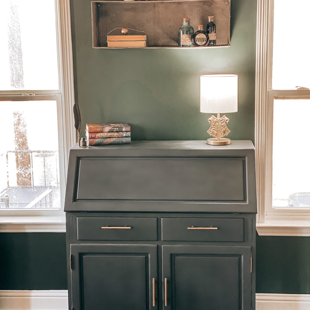 Vintage desk painted with charcoal Behr Chalk paint and antique brass drawer pulls decorated with a Hogwarts crest desk lamp, an ink quill and Harry Potter books | The Yellow Rose Farmhouse | www.theyellowrosefarmhouse.com