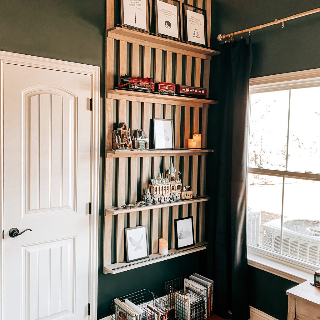 Another view of our DIY Wood Slat Accent Wall with shelves stained with weathered oak stain and painted black railing on dark green walls in Harry Potter inspired boy's bedroom. Shelves are decorated with Harry Potter Legos, Harry Potter Quotes, the Hogwarts Castle, The Hogwarts Express, candles & books. | The Yellow Rose Farmhouse | www.theyellowrosefarmhouse.com