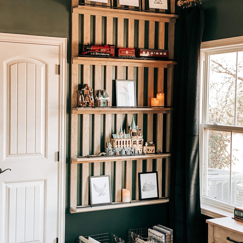 DIY Wood Slat Accent Wall with shelves stained with weathered oak stain and painted black railing on dark green walls in Harry Potter inspired boy's bedroom. Shelves are decorated with Harry Potter Legos, Harry Potter Quotes, the Hogwarts Castle, The Hogwarts Express, candles & books. | The Yellow Rose Farmhouse | www.theyellowrosefarmhouse.com