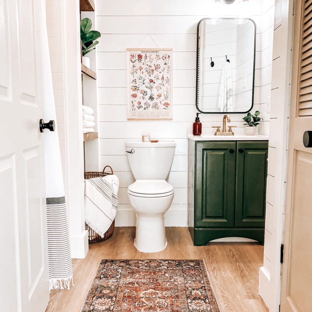 Modern Farmhouse Bathroom with views of vintage wall art, painted vanity, champagne bronze fixtures, farmhouse lighting, shiplap walls and louvered solid wood door | The Yellow Rose Farmhouse | www.theyellowrosefarmhouse.com