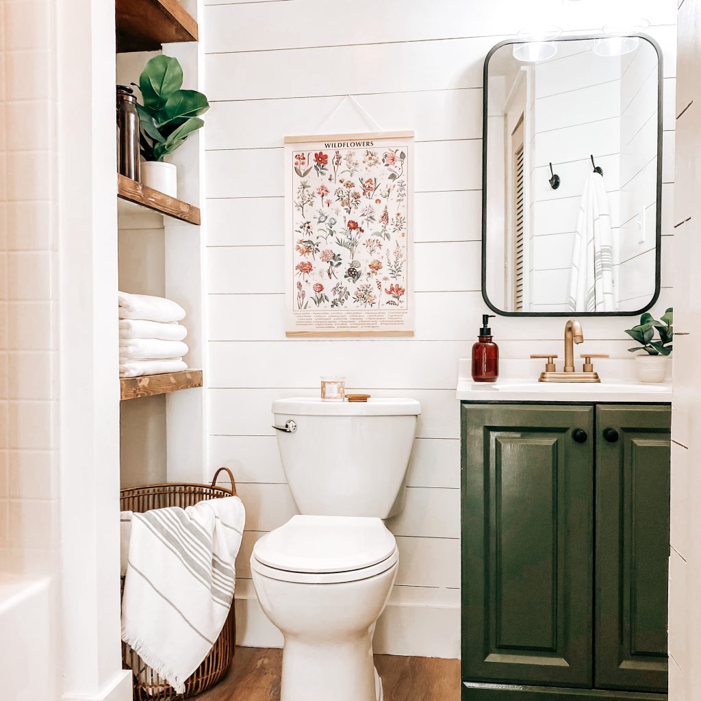 Modern Farmhouse Bathroom with views of vintage wall art, painted vanity, champagne bronze fixtures, farmhouse lighting, shiplap walls and louvered solid wood door | The Yellow Rose Farmhouse | www.theyellowrosefarmhouse.com